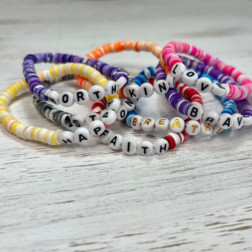 Set of colorful beaded bracelets with letter beads on a light wooden surface