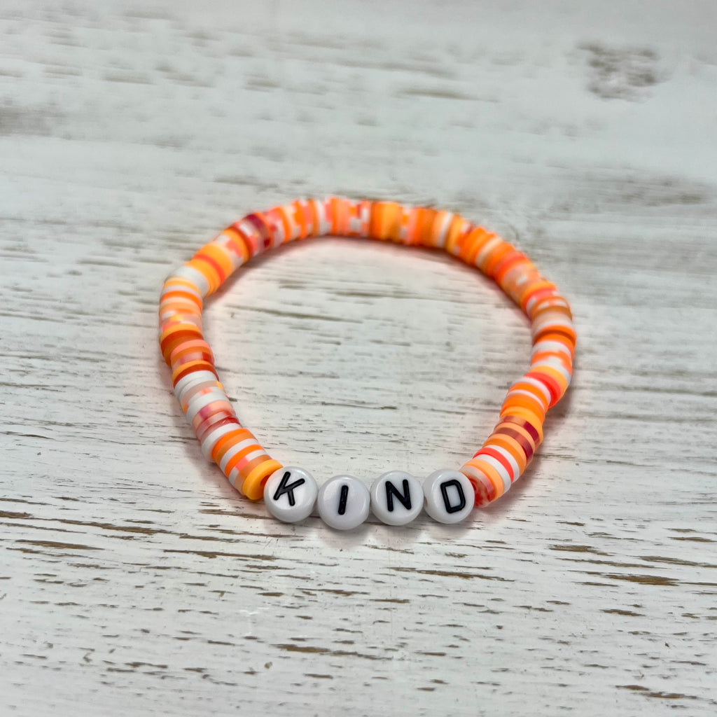 Colorful beaded bracelet with letter beads spelling 'KIND' on a wooden surface