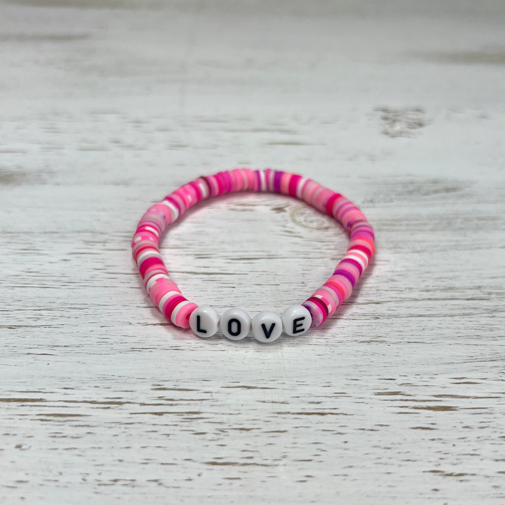 Pink and white beaded bracelet with 'LOVE' beads on a wooden surface