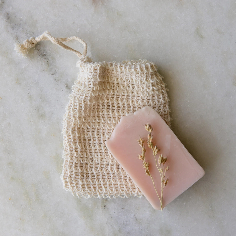 Pink soap with dried herbs on a natural fiber bag against a marble background