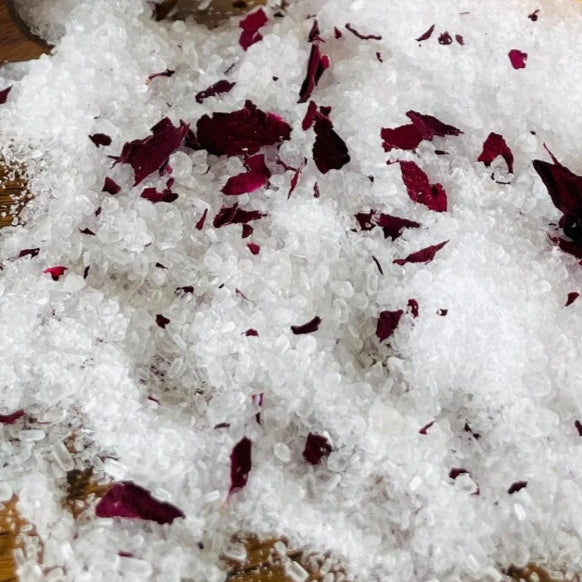 White bath salt with red flower petals on a wooden surface