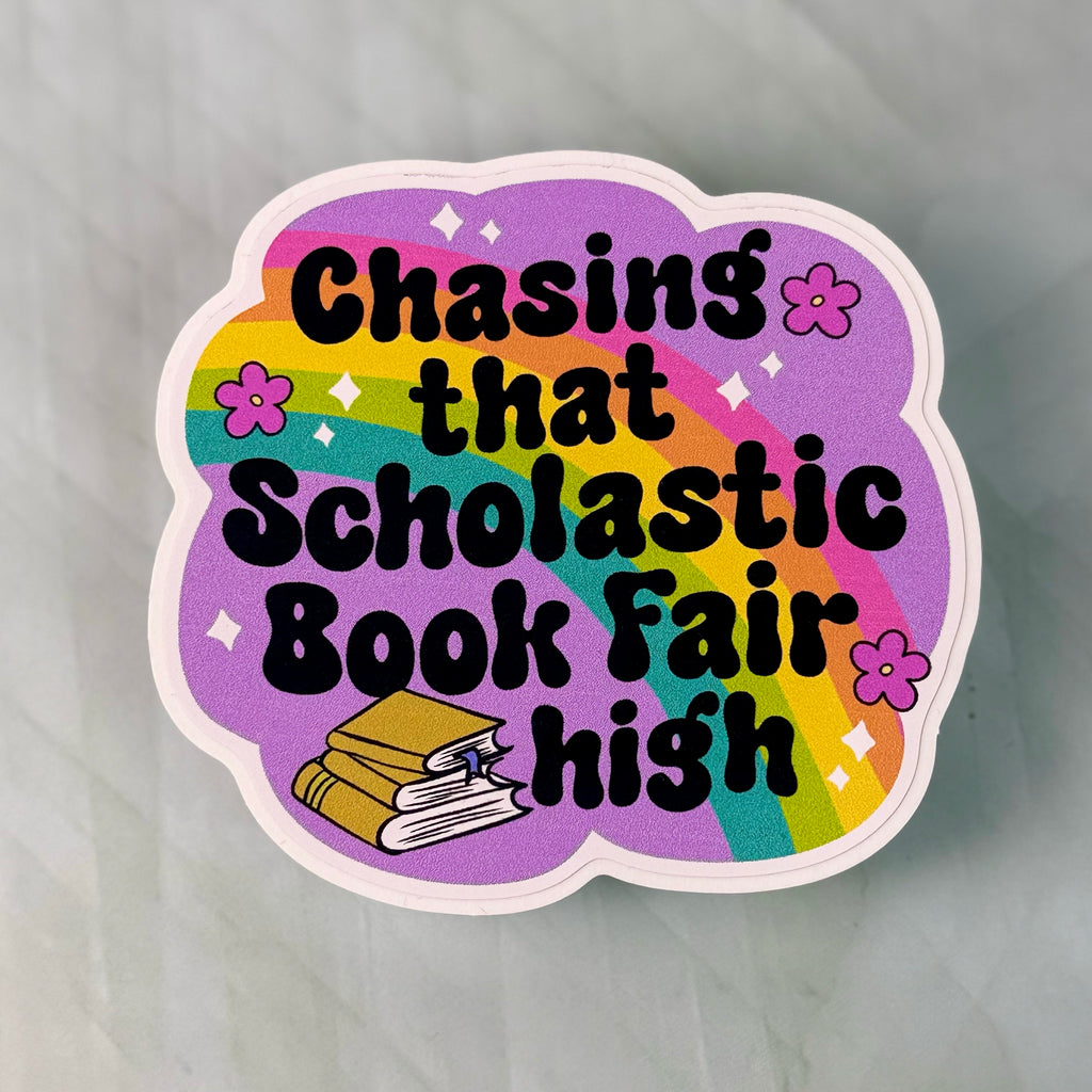 Sticker with rainbow design and text 'Chasing that Scholastic Book Fair high' on a gray background