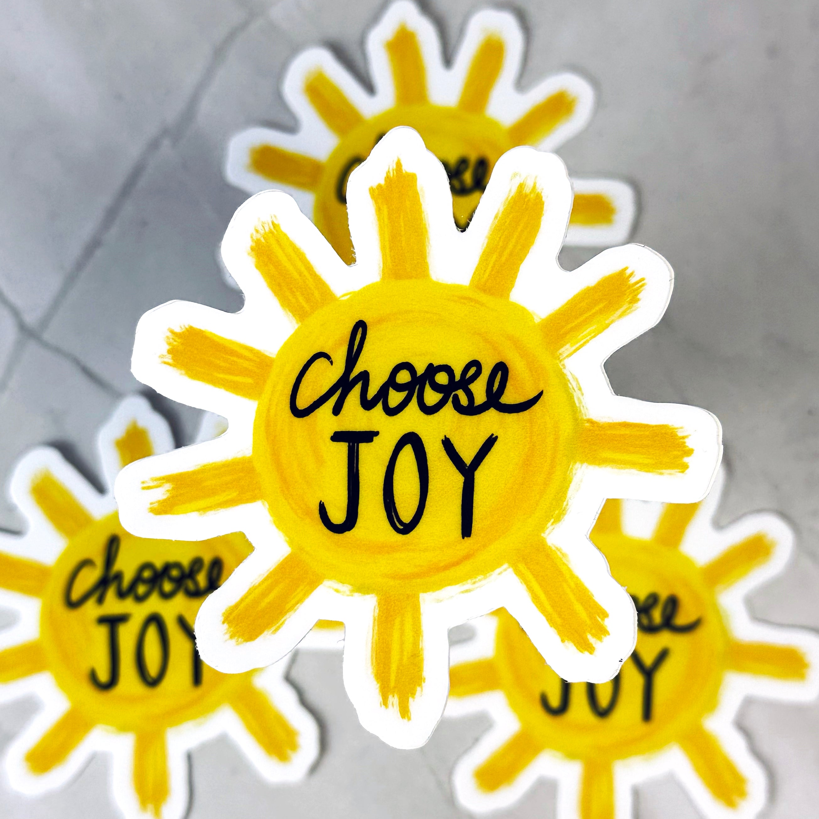 Sun-shaped stickers with 'Choose Joy' text on a gray background