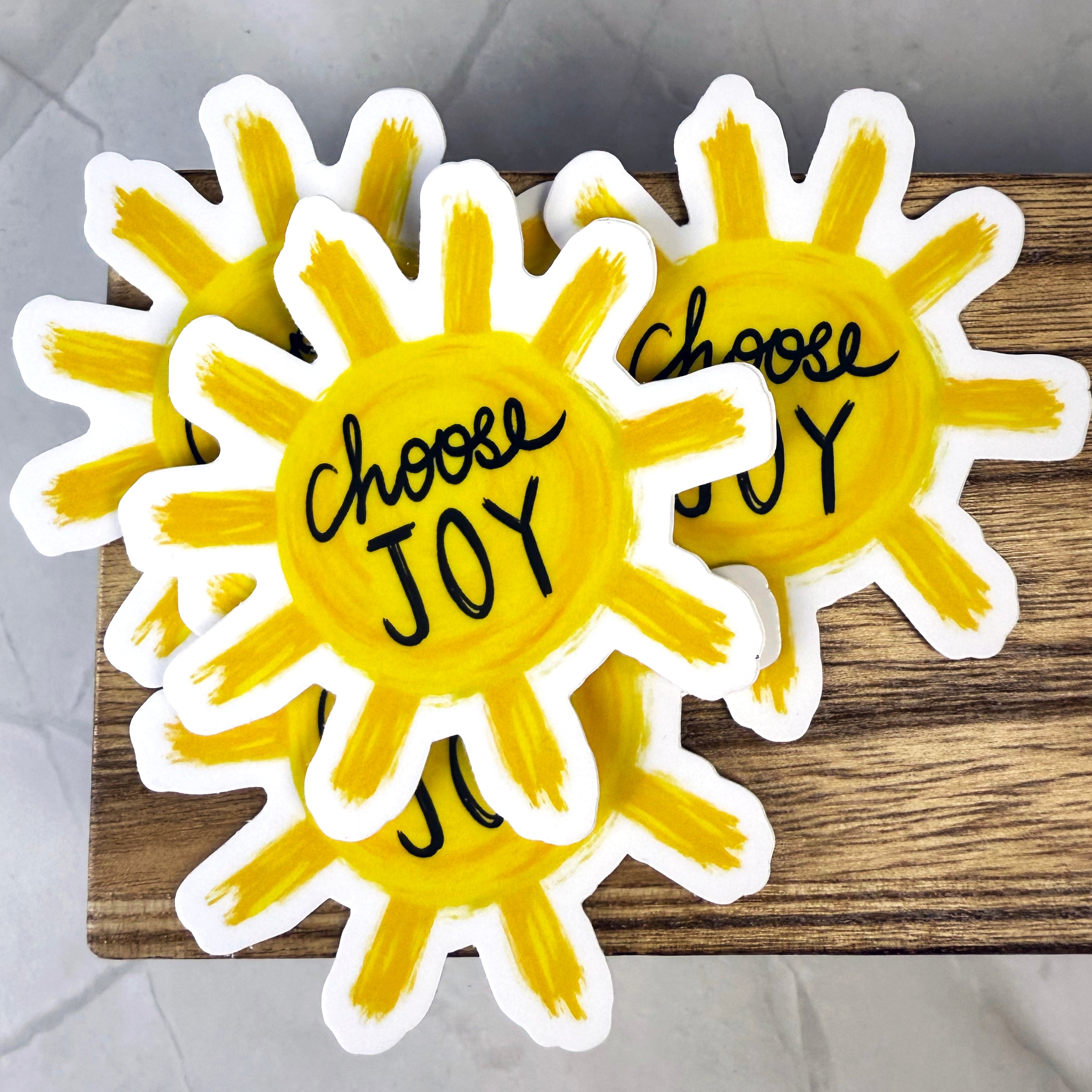 Two sun-shaped stickers with 'Choose Joy' text on a wooden surface.