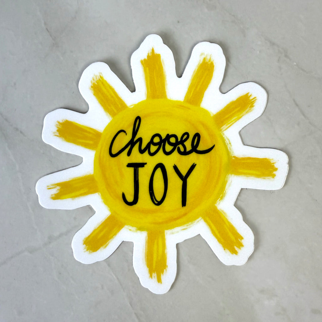 Sun-shaped sticker with 'Choose Joy' text on a gray background