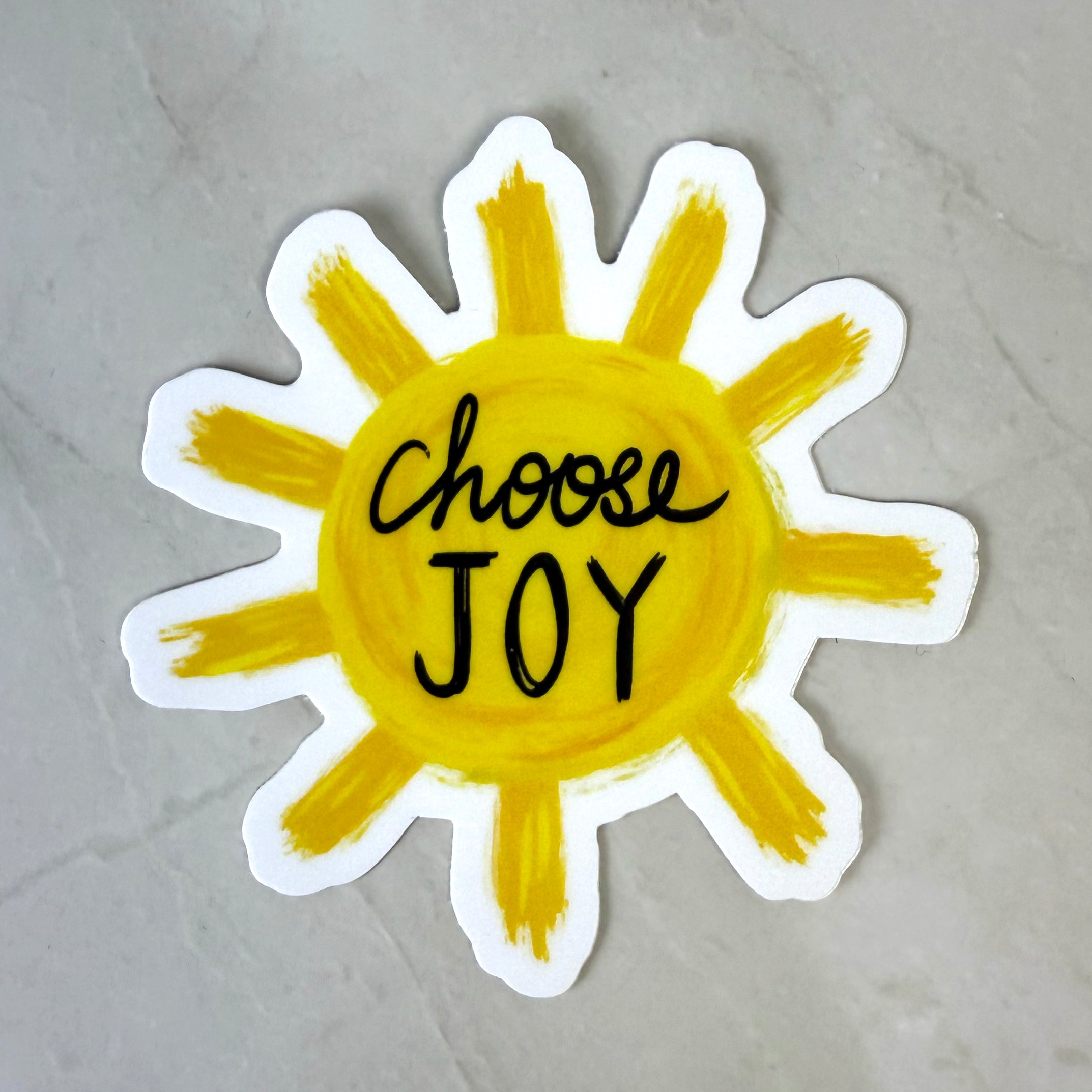 Sun-shaped sticker with 'Choose Joy' text on a gray background