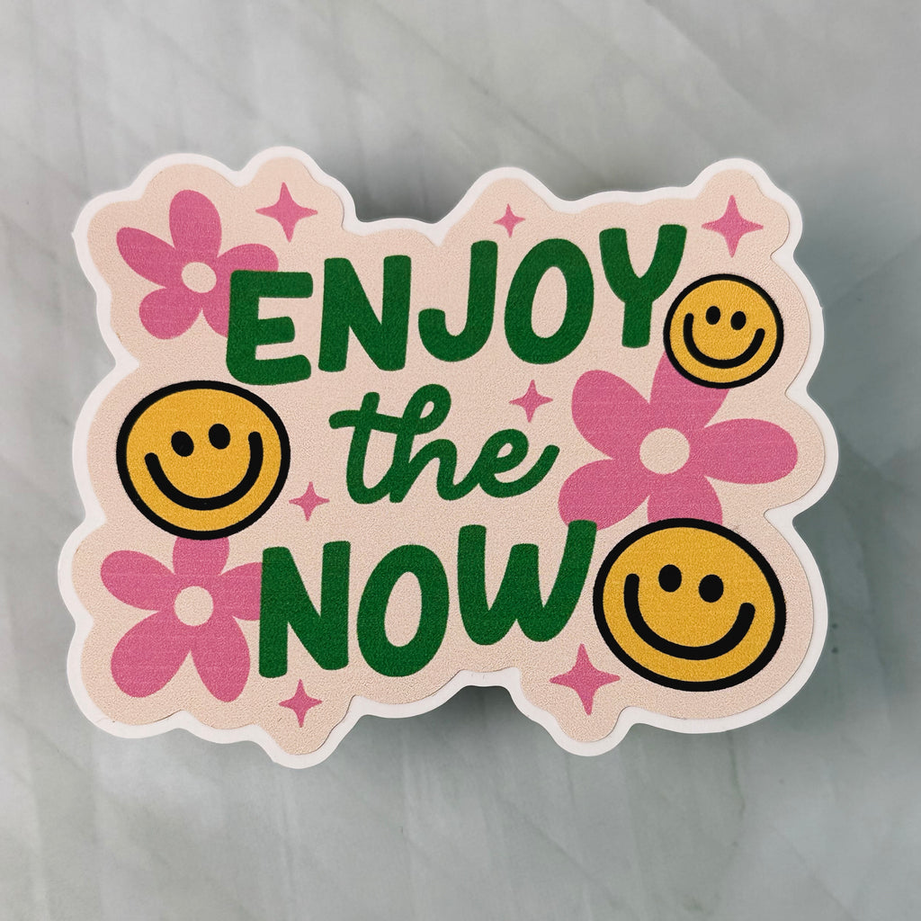 Sticker with 'ENJOY the NOW' text and smiley faces on a gray background