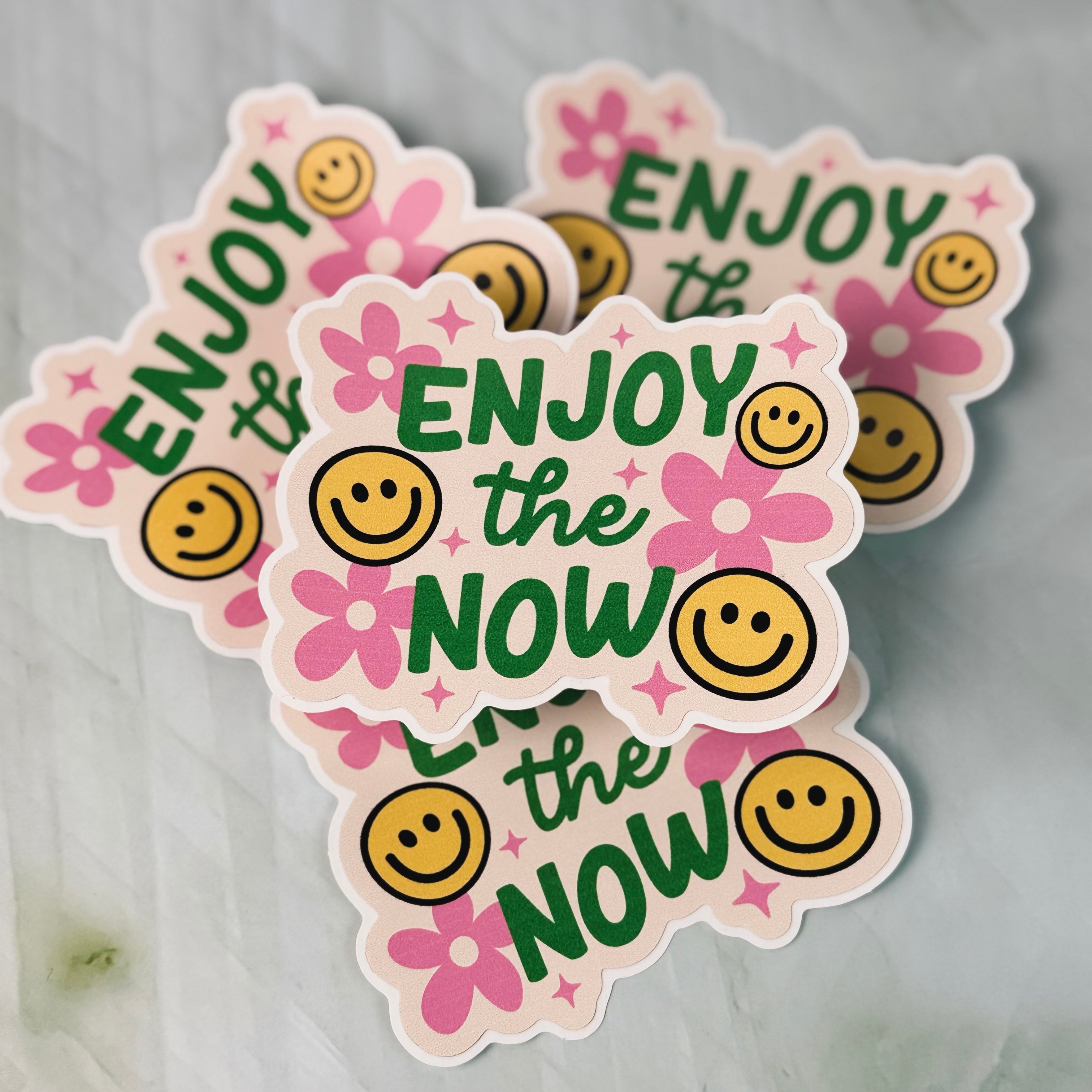 Stickers with 'Enjoy the Now' text and smiley faces on a gray background