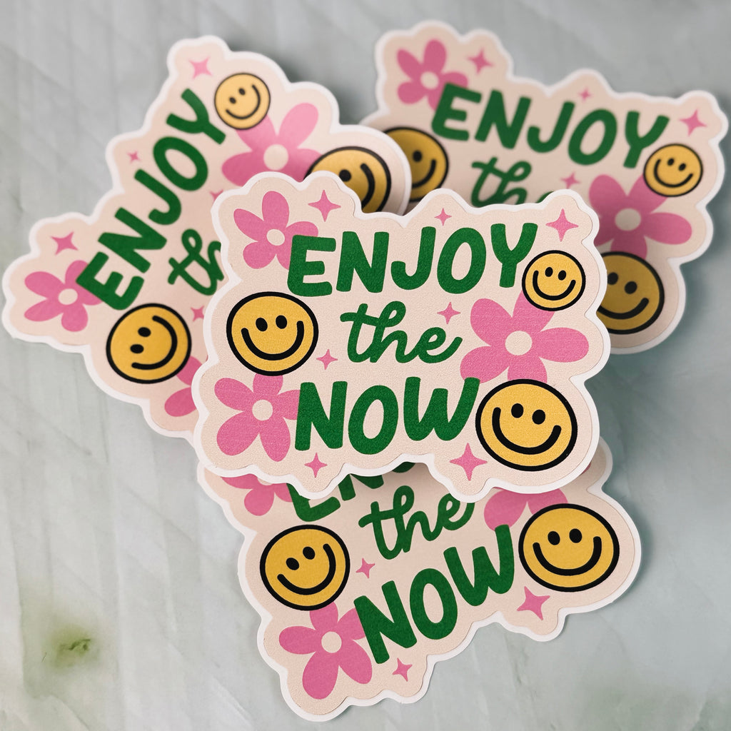 Three stickers with 'Enjoy the Now' text and smiley faces on a light gray background