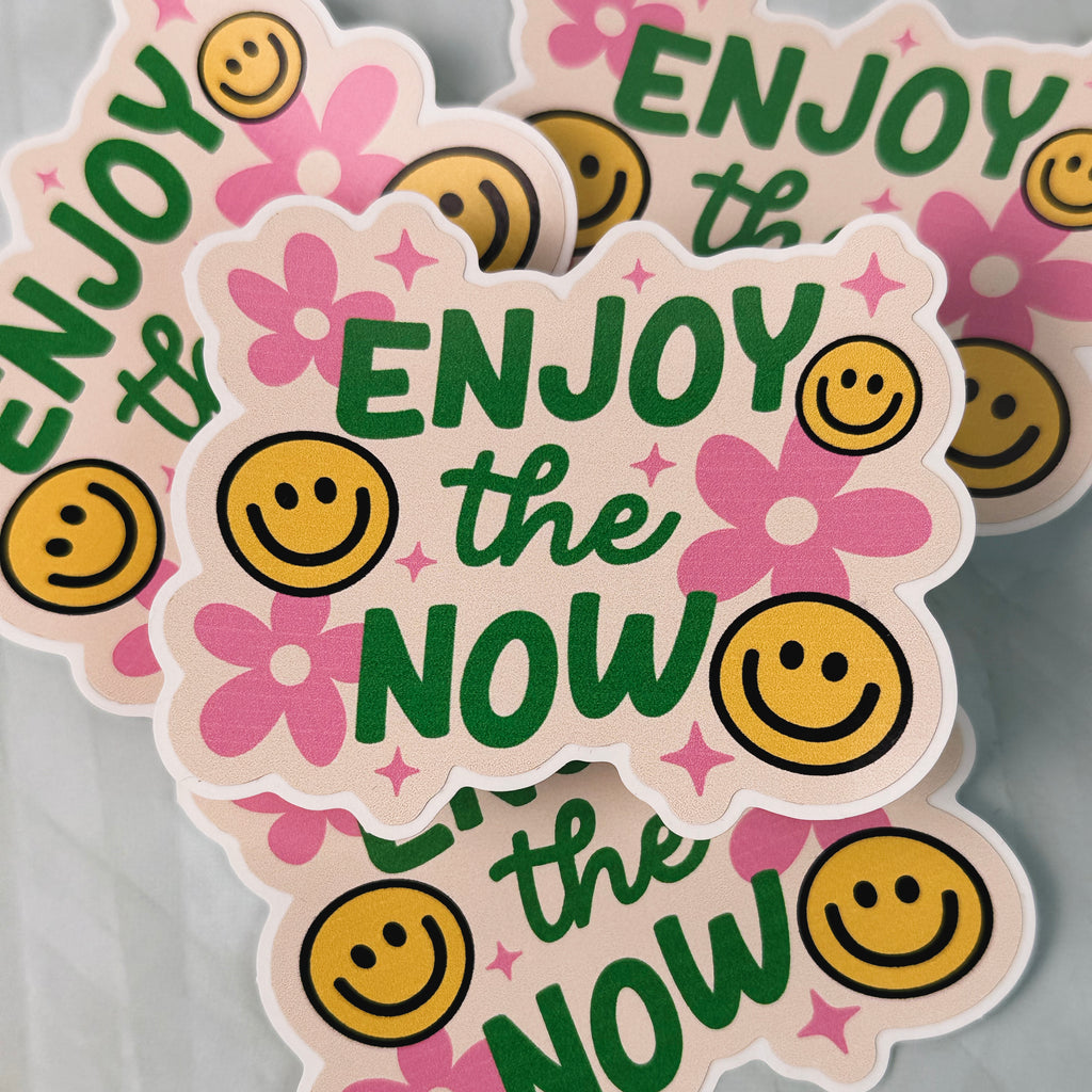 Stickers with 'Enjoy the Now' text and smiley faces on a gray background