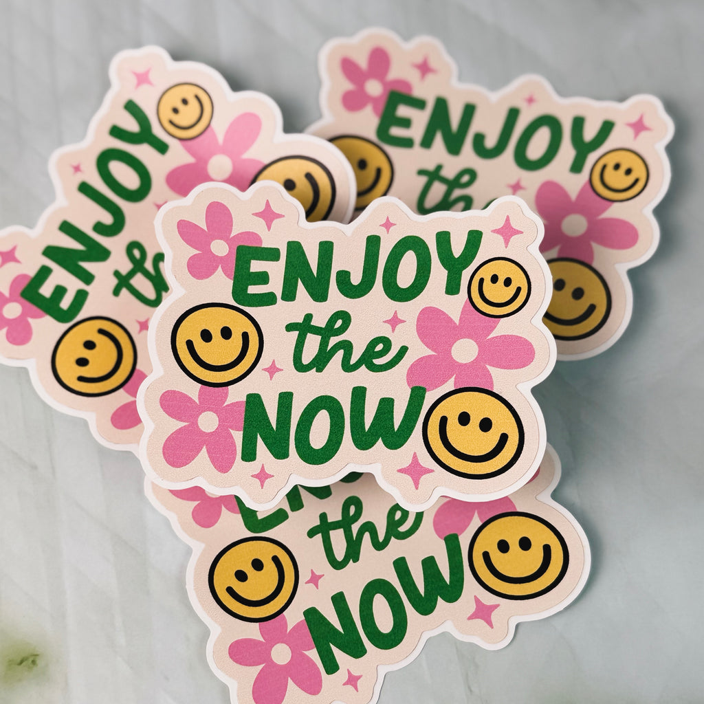 Stickers with 'Enjoy the Now' text and smiley faces on a gray background