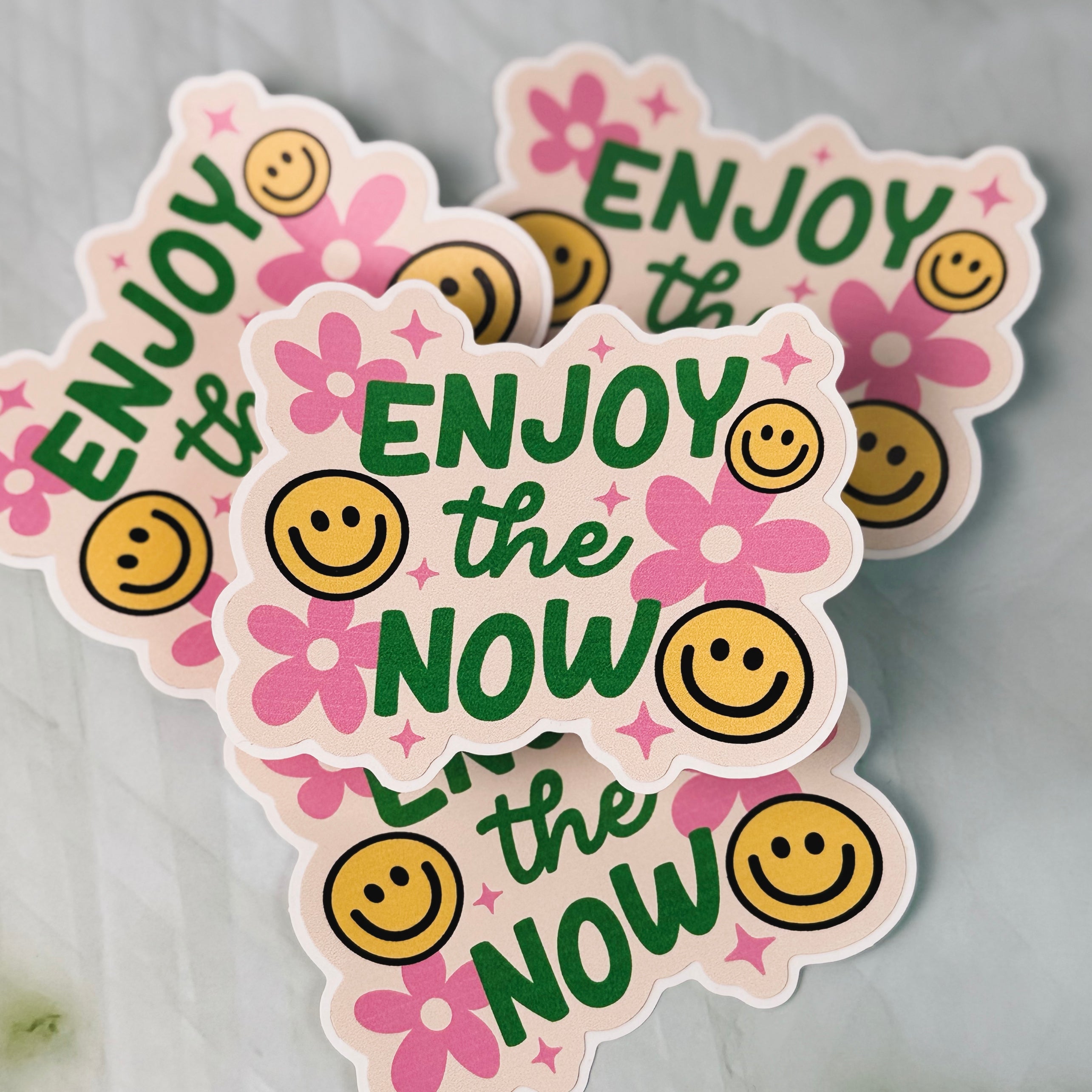 Stickers with 'Enjoy the Now' text and smiley faces on a gray background