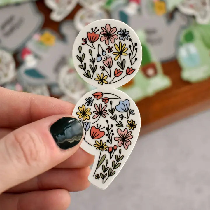 Hand holding two floral-patterned stickers with a blurred background of more stickers.