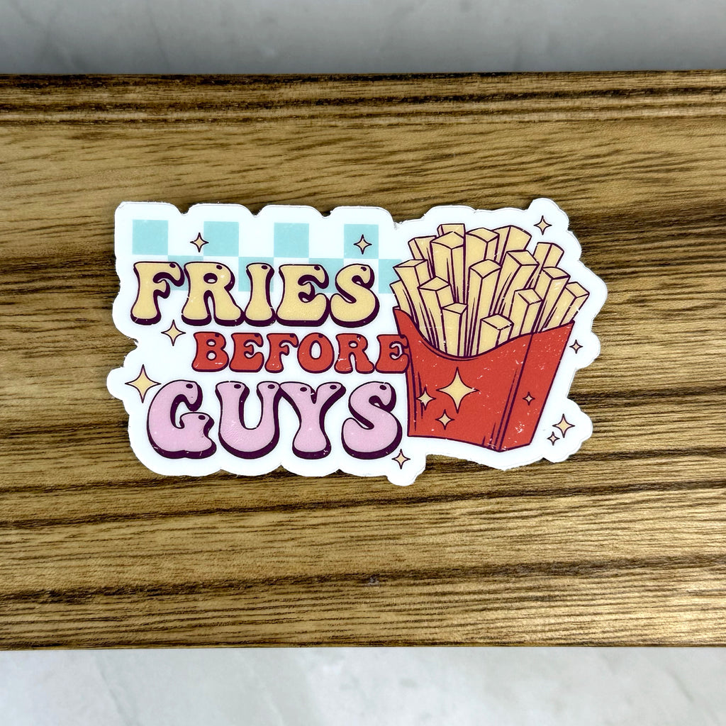 Sticker with 'Fries Before Guys' text on a wooden surface