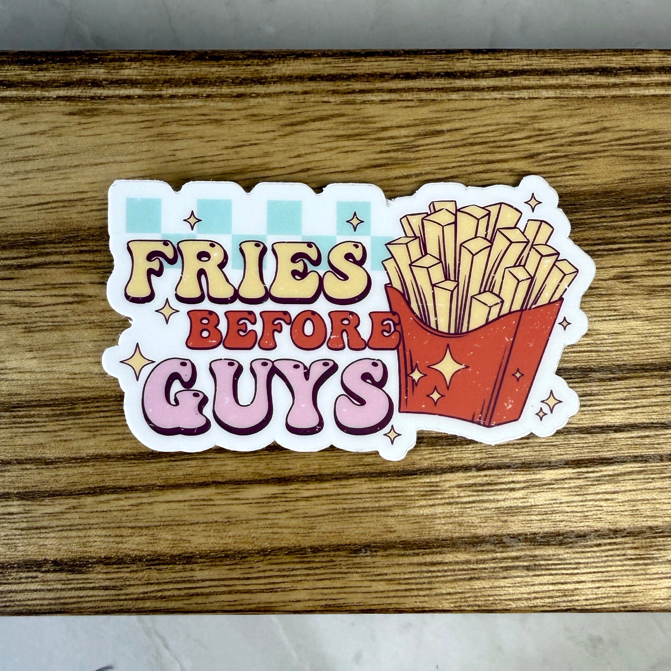 Sticker with 'Fries Before Guys' text and a graphic of fries on a wooden surface