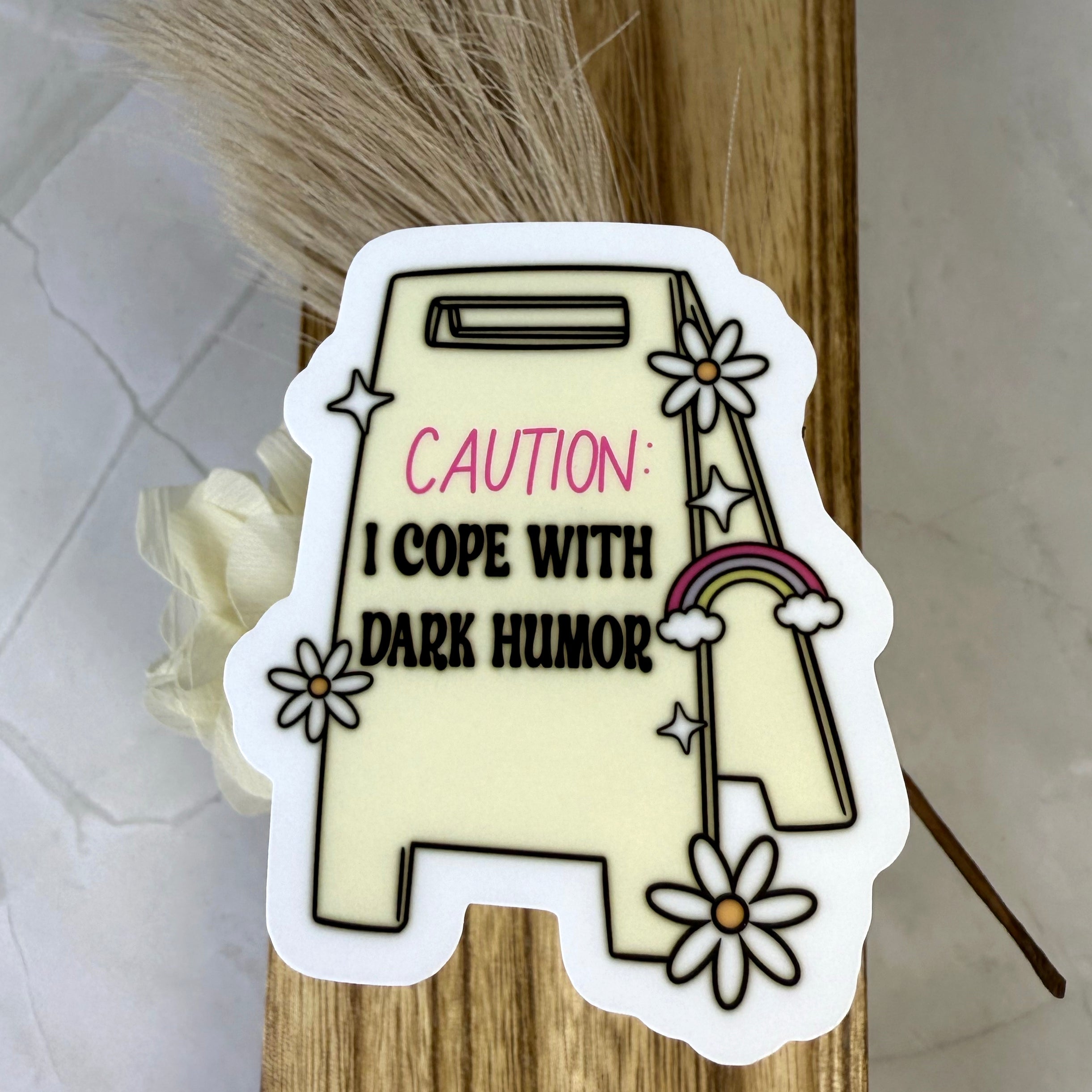 Sticker with text 'Caution: I cope with dark humor' on a wooden background