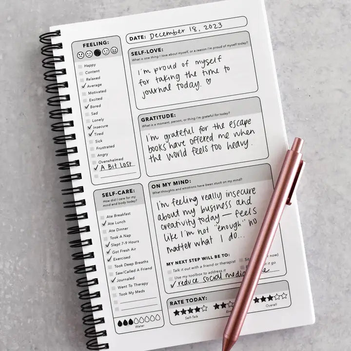 Journal with daily reflections and a pen on a gray surface