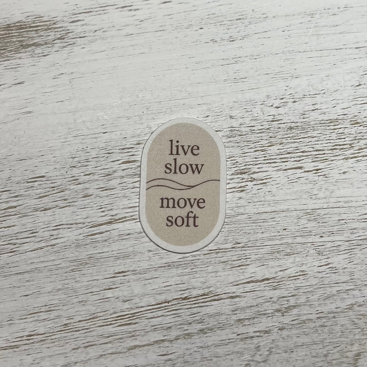 Sticker with 'live slow move soft' text on a wooden surface