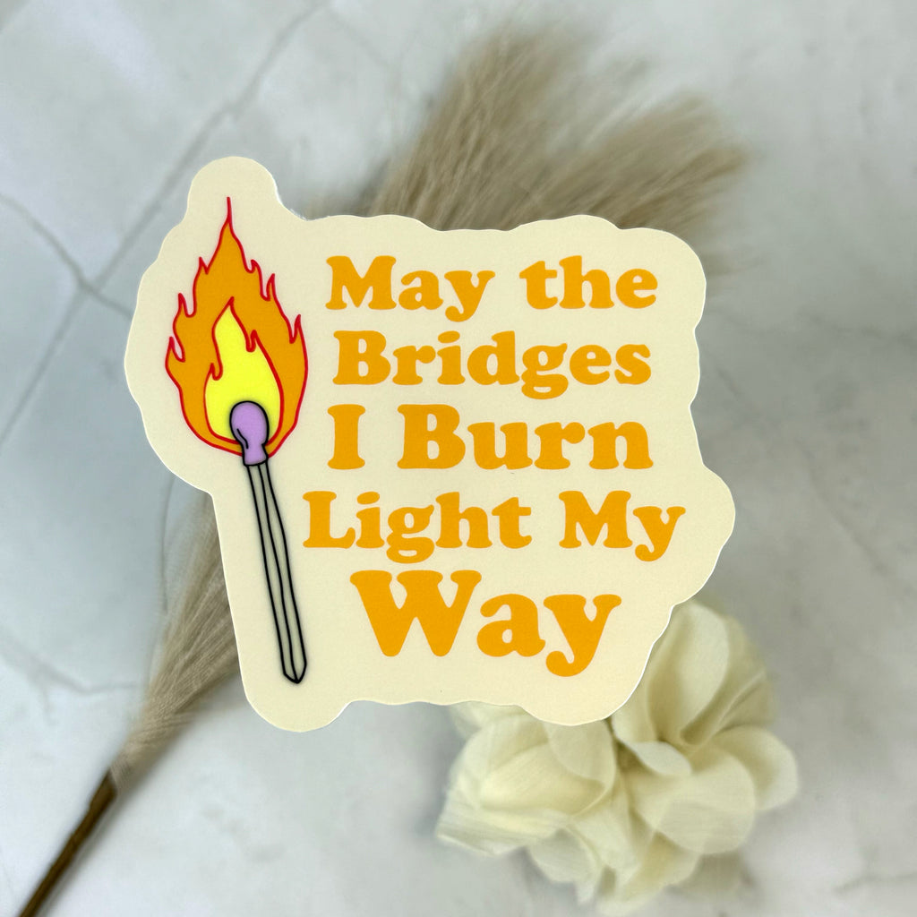 Sticker with a match and text 'May the Bridges I Burn Light My Way' on a light background.