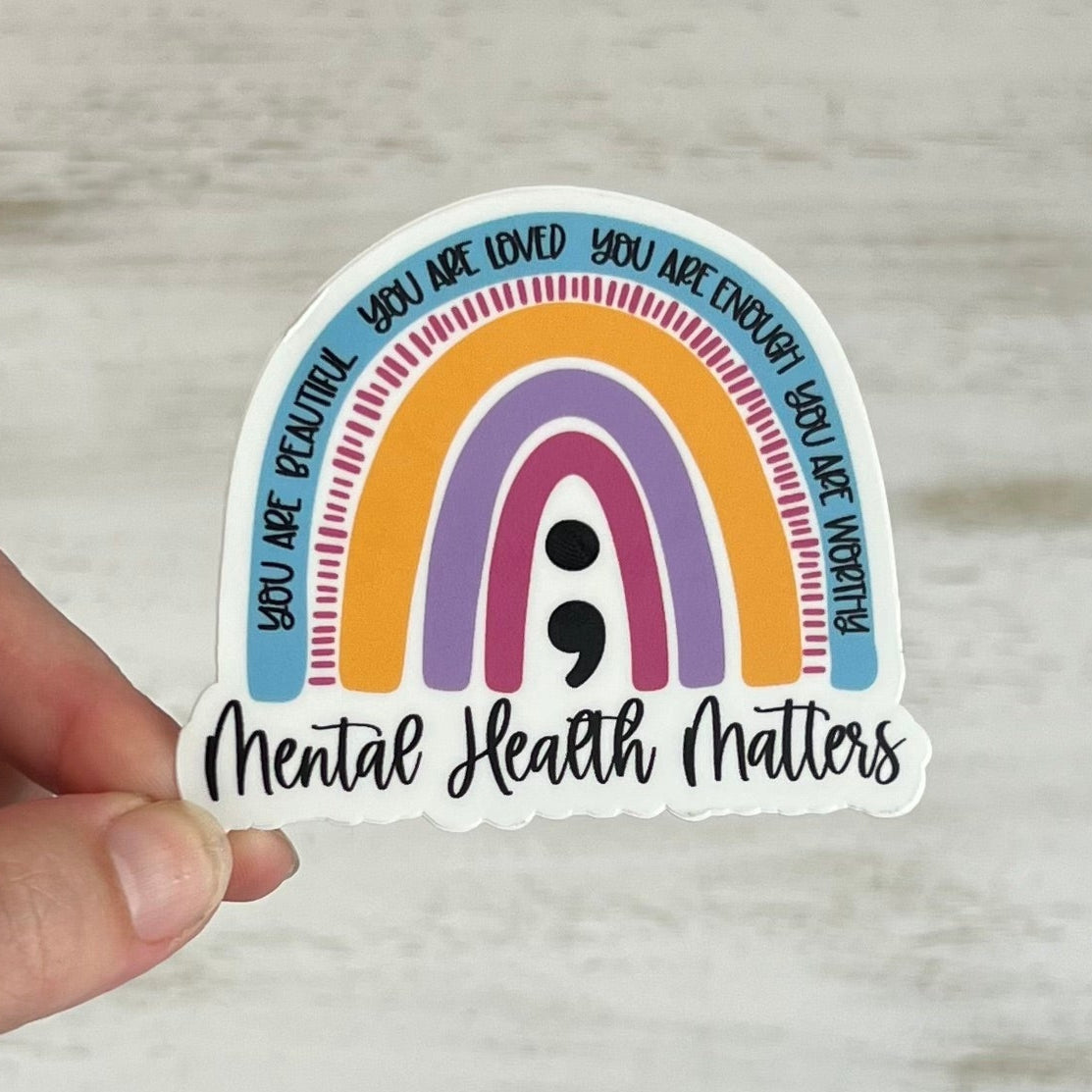 Sticker with rainbow design and motivational text held by a hand on a light wooden surface