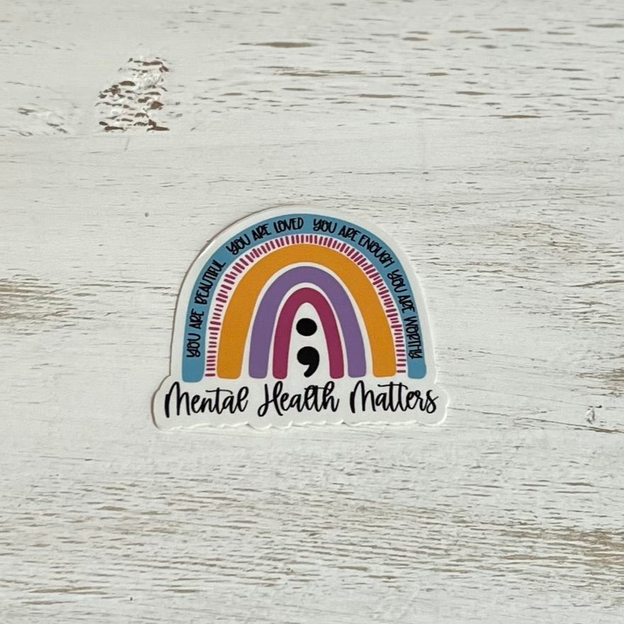 Sticker with rainbow design and 'Mental Health Matters' text on a wooden surface