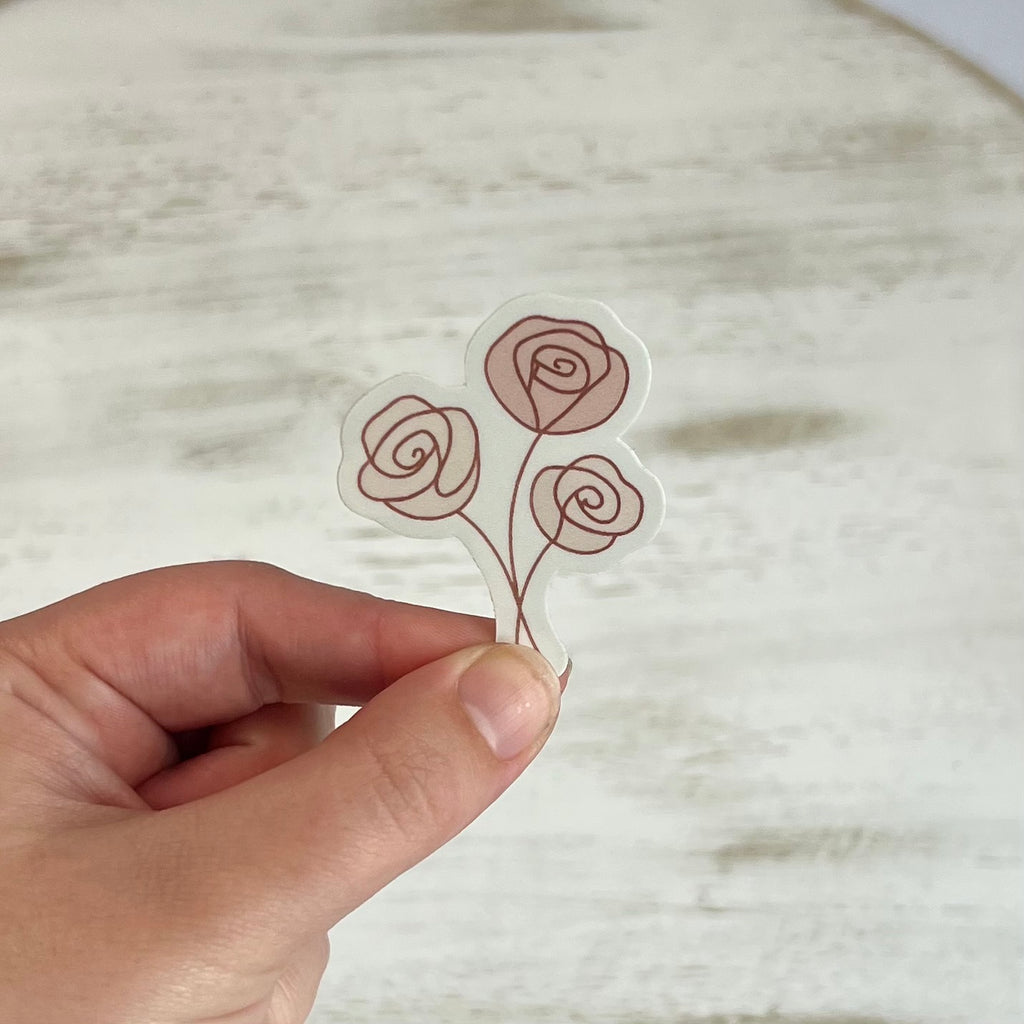 Hand holding a clear sticker with red rose designs against a neutral background