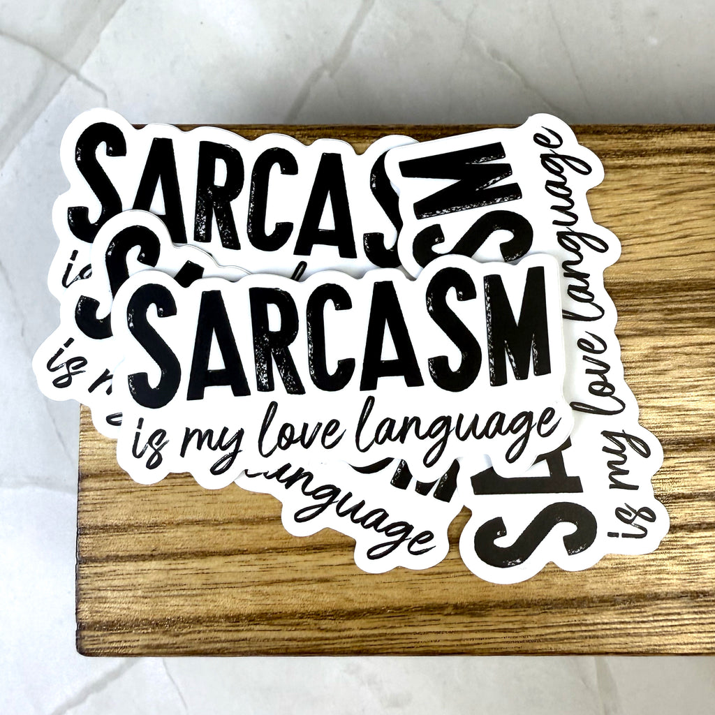 Sticker with text 'Sarcasm is my love language' on a wooden surface
