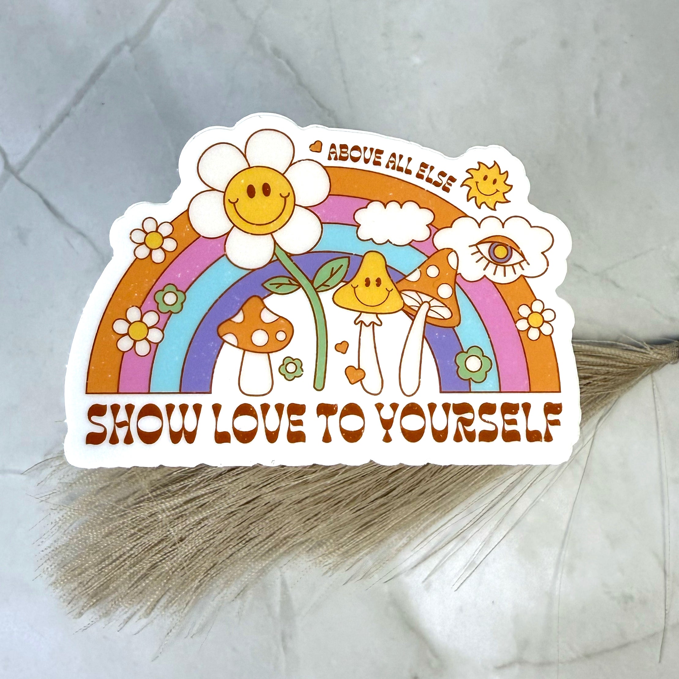 Sticker with a rainbow, flowers, and mushrooms on a gray surface