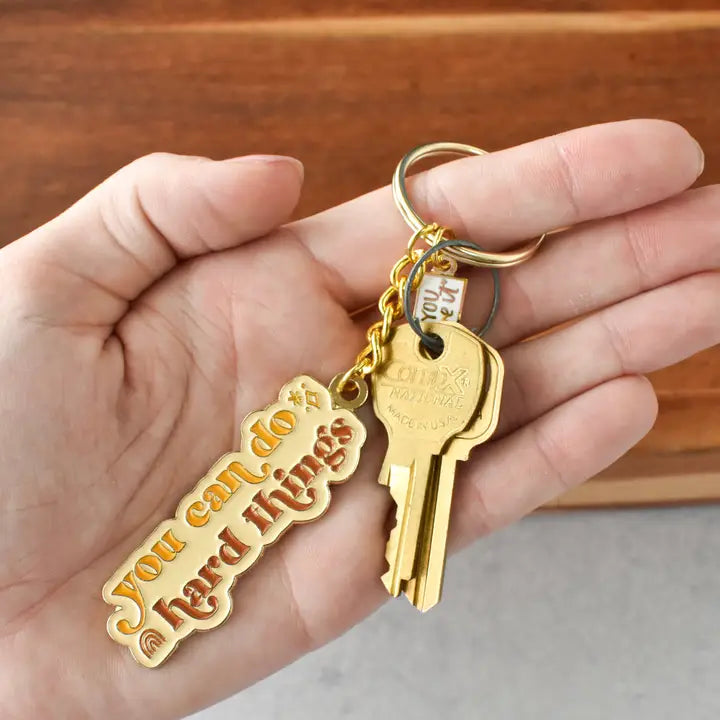 Hand holding a key with a motivational keychain against a wooden background
